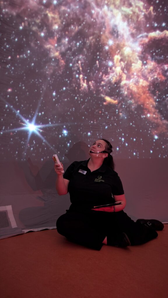 Toni, sitting on the floor of a portable planetarium, looking up at the stars projected onto the dome.